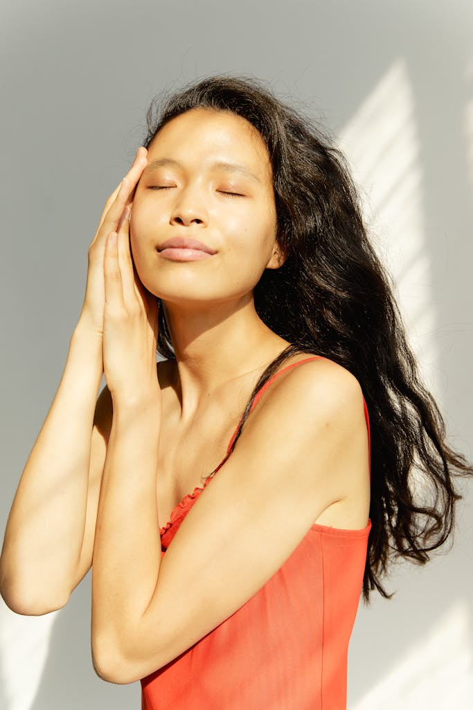 A serene studio portrait of a young woman in a red dress, eyes closed, relaxed pose.