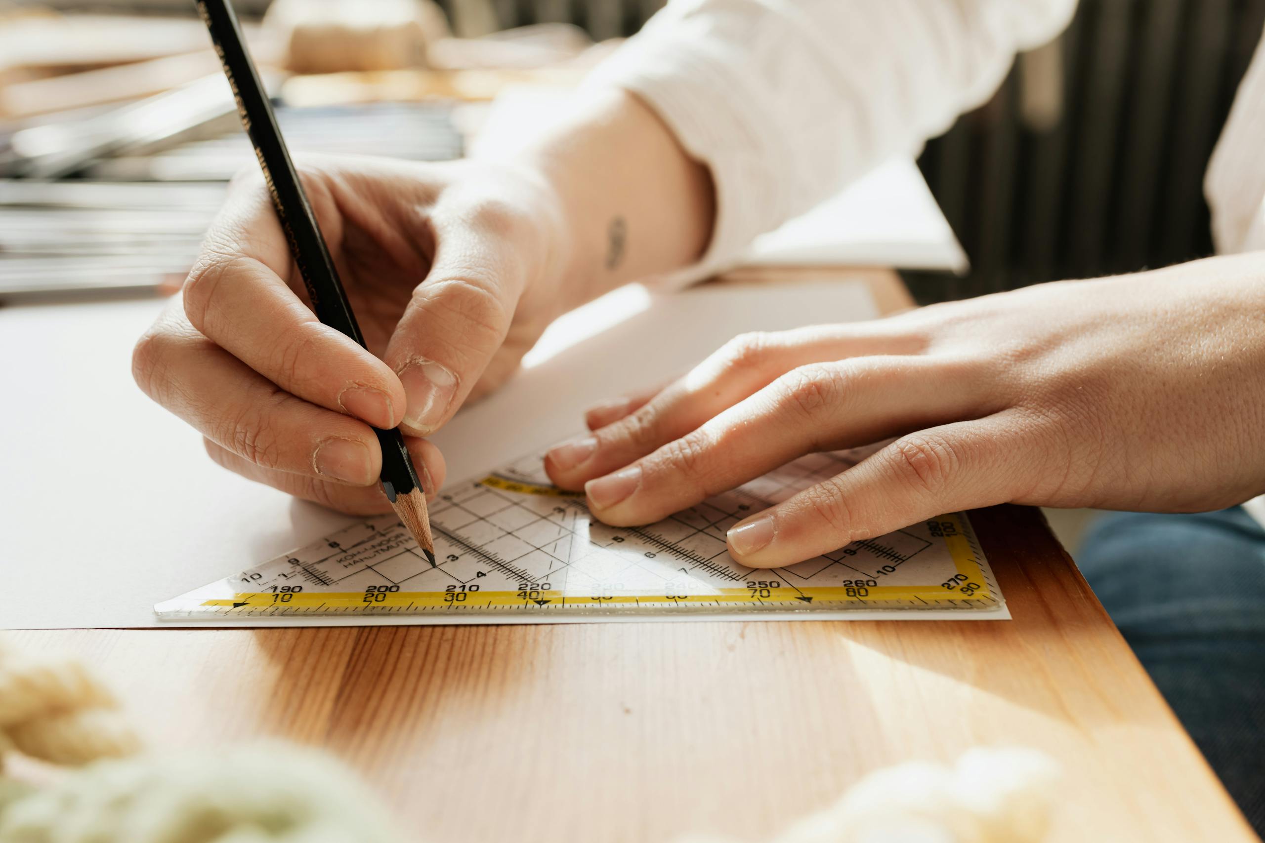 Close-up of hands sketching with pencil and ruler on paper, highlighting craftsmanship.