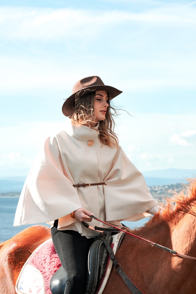 Woman in elegant attire on horseback with a scenic outdoor backdrop.